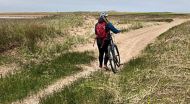 Image d'une jeune femme de dos qui marrche à côté de son vélo dans un un sentier